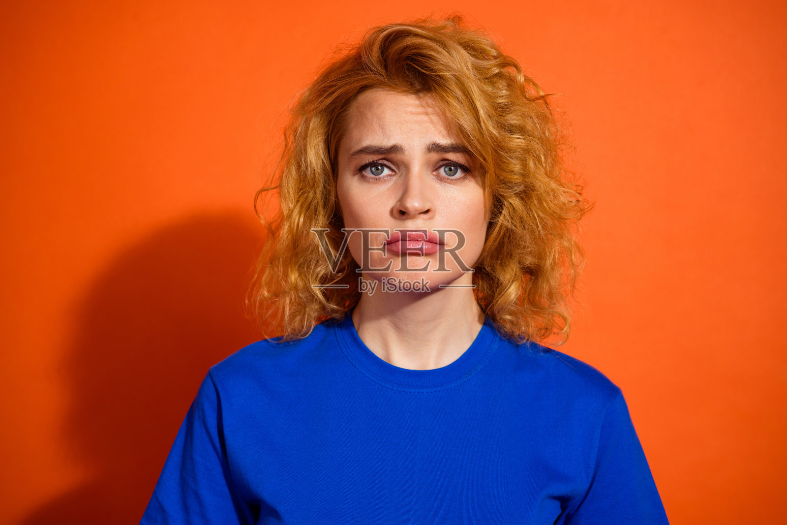 一位年轻女性的肖像，她有着卷曲的红发，穿着蓝色T恤，随意地在橙色背景前摆姿势。照片摄影图片