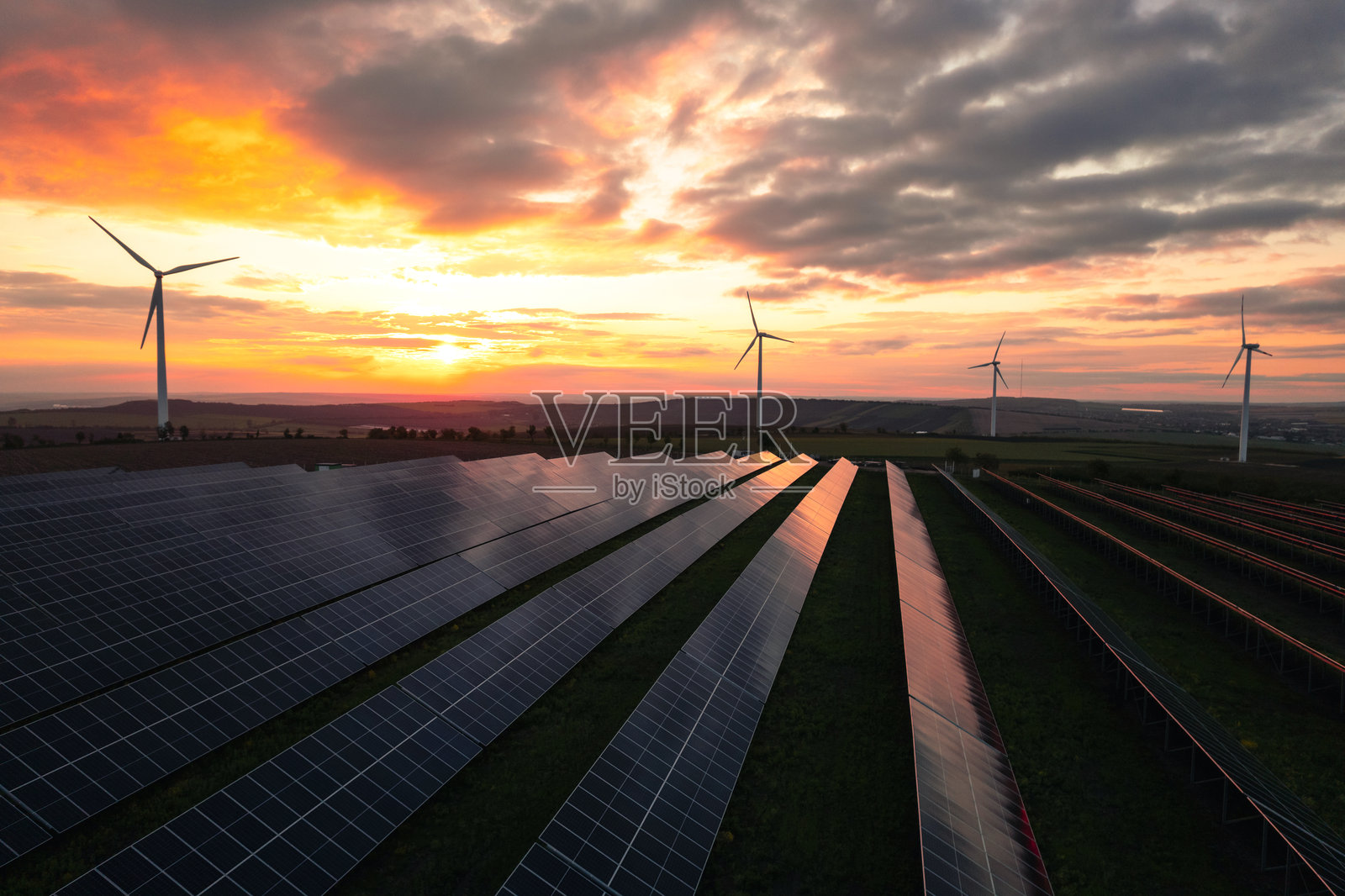 风力发电机公园的鸟瞰图，产生绿色能源电力。日落时分的太阳能电池板公园和风力涡轮机。绿色能源减少碳排放，使地球更清洁、更生态。照片摄影图片