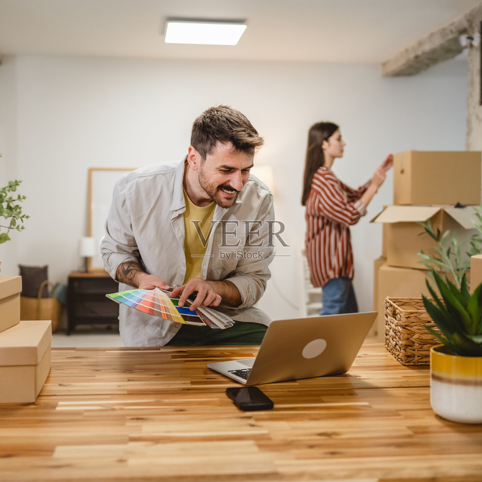 男子在视频通话中展示色板，女子则在旁边拆包。照片摄影图片