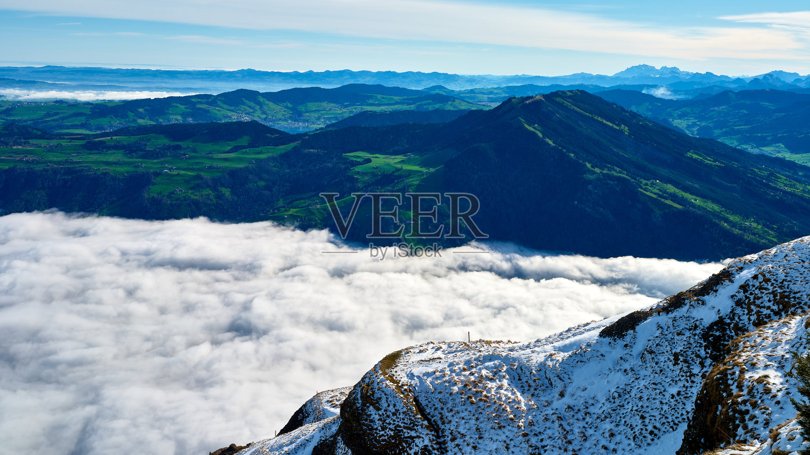 阳光明媚的山地风景，雪与云朵交织，附近是郁郁葱葱的绿色山谷，营造出宁静的环境。照片摄影图片