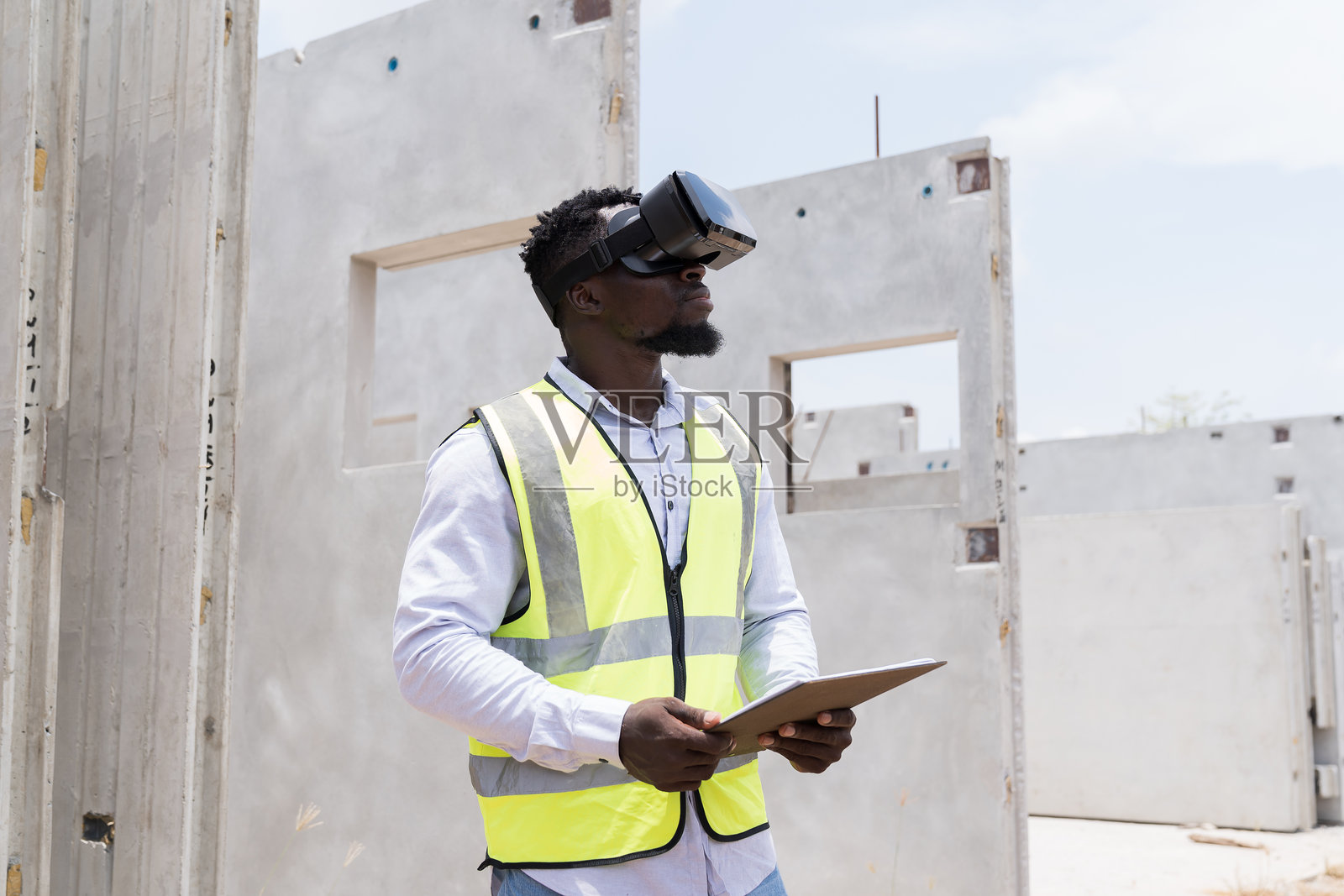 建筑工程师佩戴虚拟现实头盔，在施工现场检查预制混凝土墙的结构质量。工地上的工头正在使用虚拟现实头盔进行工作。照片摄影图片