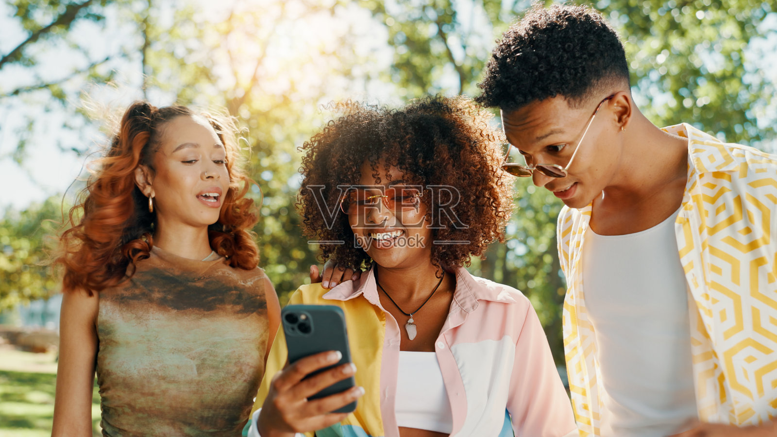 朋友们在公园里开心地展示手机，讨论社交媒体八卦、网络剧和互联网新闻。Z世代的人们放松地使用智能手机，获取惊喜信息、网络公告和短信通知。照片摄影图片