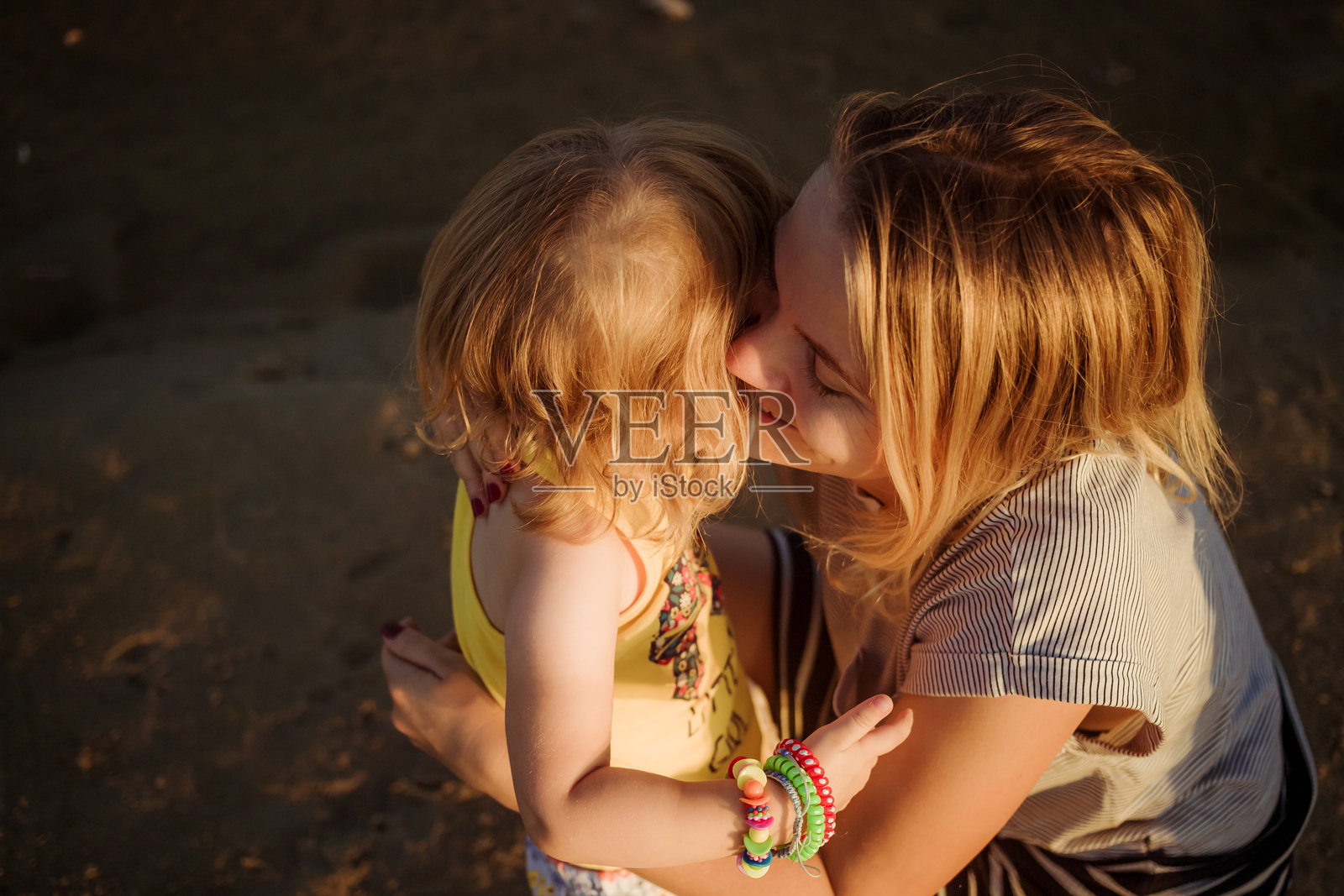 微笑的妈妈在日落时分拥抱她的小女儿，轻声在她耳边低语。幸福的家庭亲子关系。爱与幸福的概念。信任与接纳。心理舒适。夏天。照片摄影图片