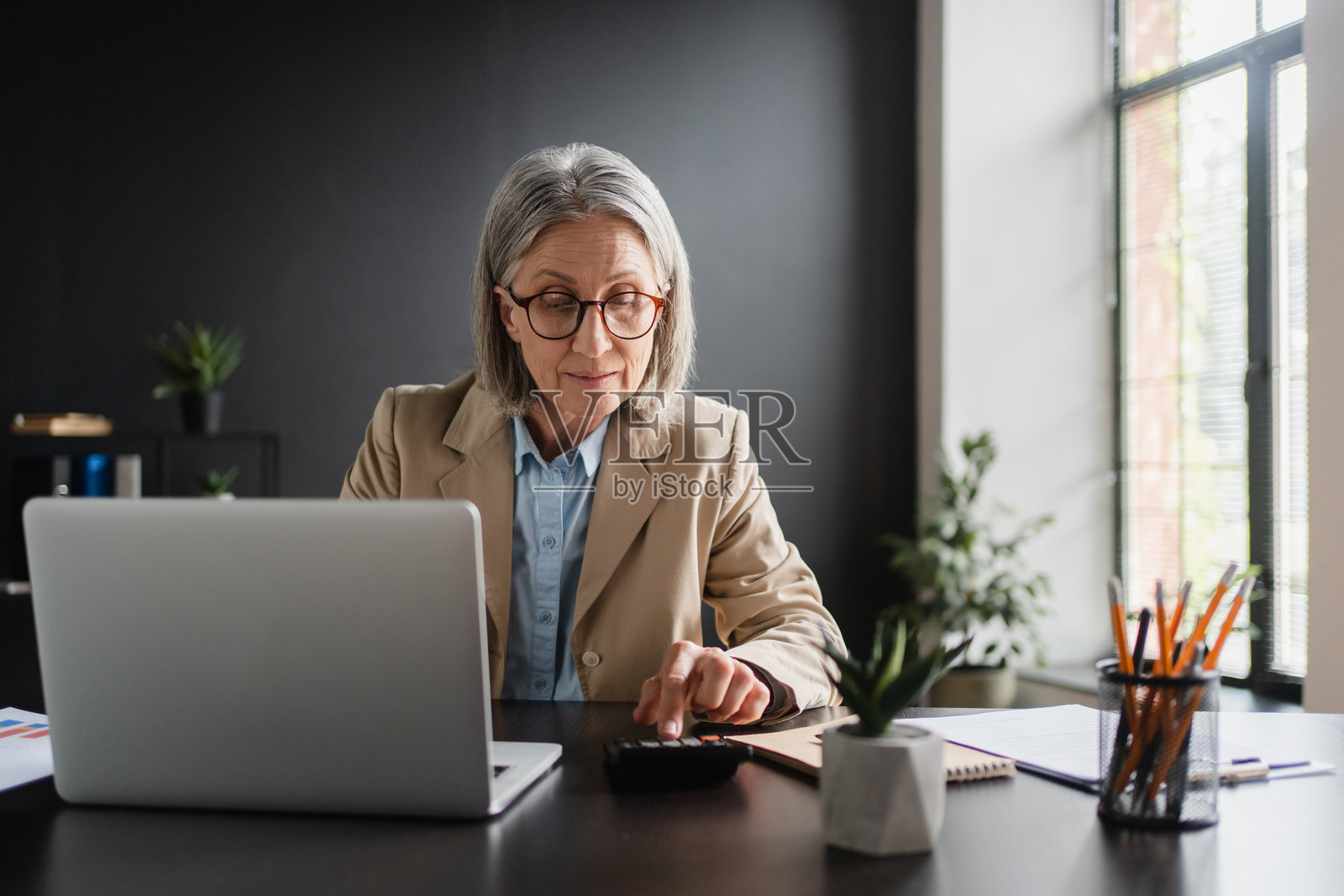 成熟的白人女性商务经理在办公室工作，进行审计分析图表公司预算报告，负责应收账款、生产控制、运营审计和成本加成定价。照片摄影图片