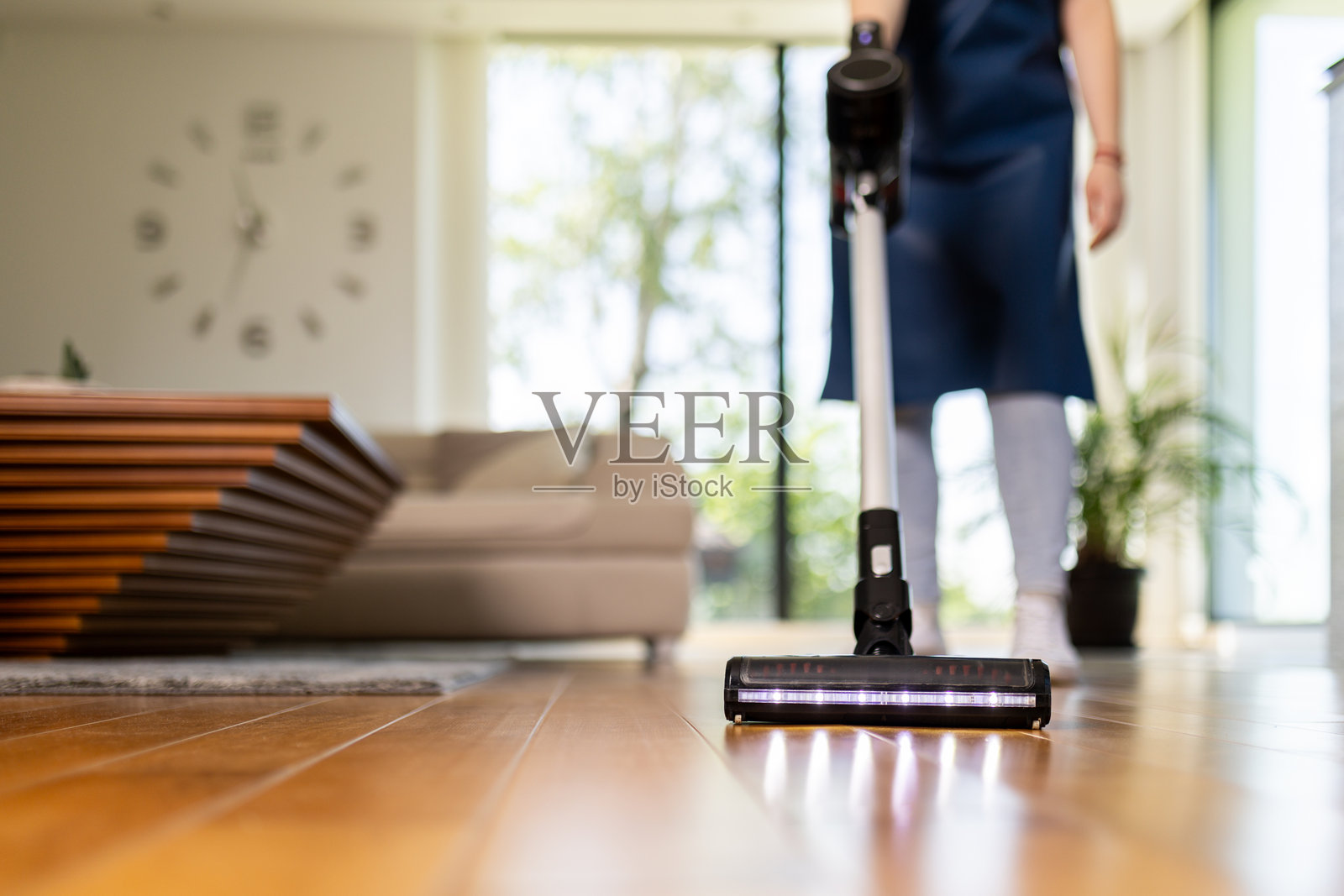 在明亮现代的客厅里，一个人正在用吸尘器清洁木地板。照片摄影图片