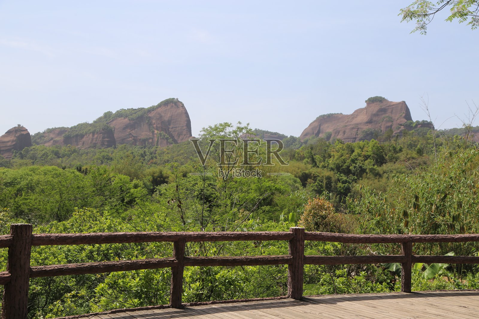 一个木质护栏的露台，地面上有绿色植物，远处有三块红色岩石。照片摄影图片