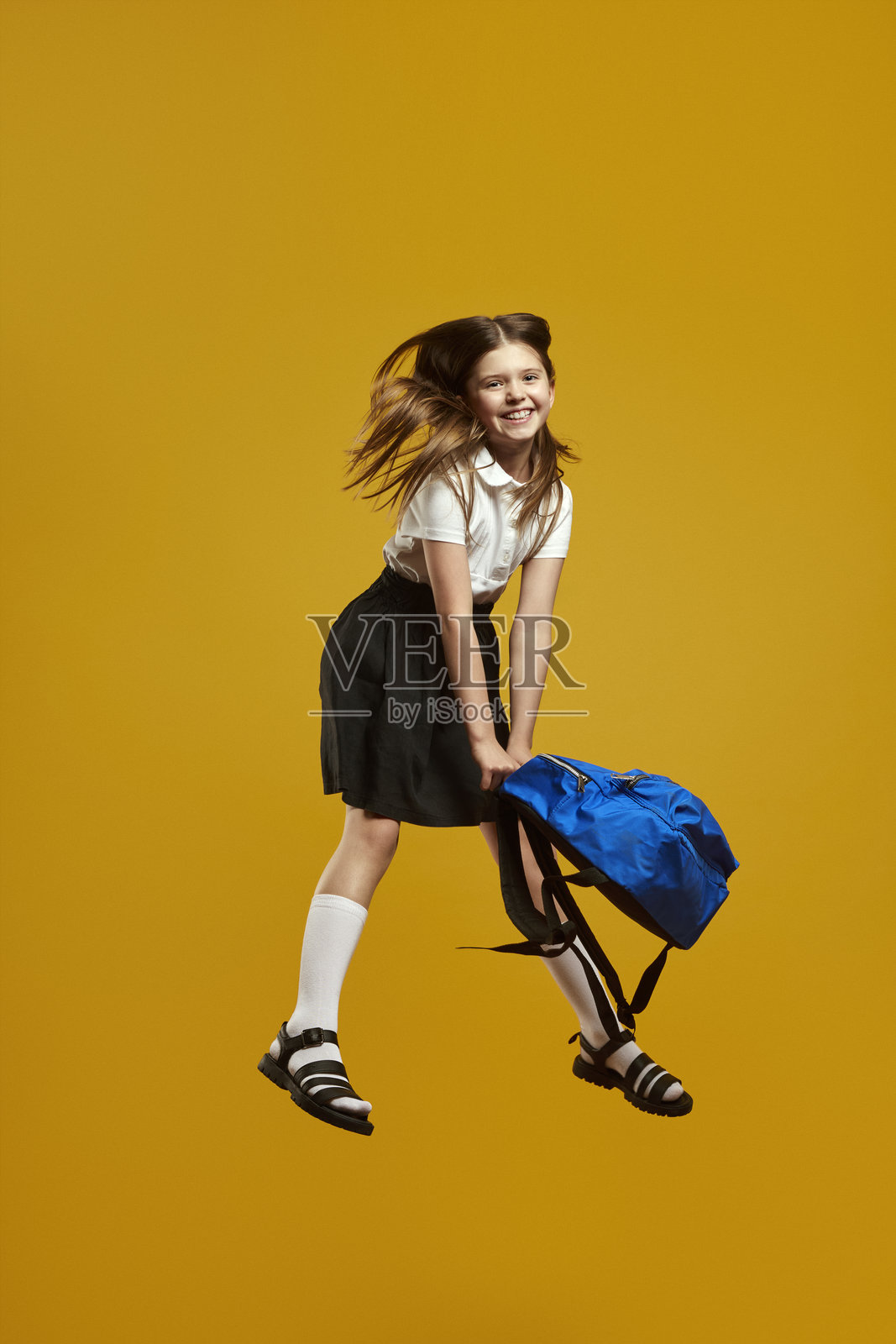 快乐的小女孩在鲜艳的黄色背景下跳跃，背着书包照片摄影图片