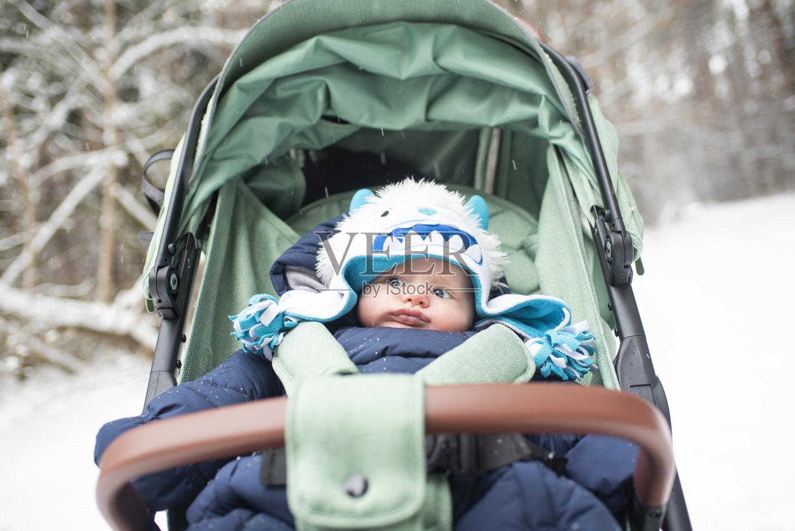 冬季雪白森林中坐在绿色婴儿车里的小男孩照片摄影图片