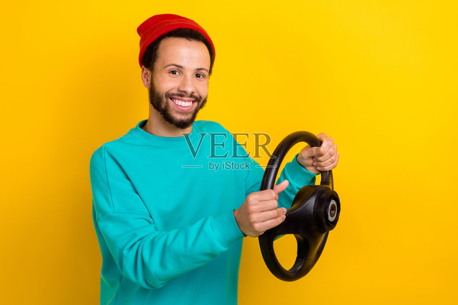 穿着青绿色毛衣的满意男子，留着胡须，手握方向盘，测试新车，背景为黄色。照片摄影图片