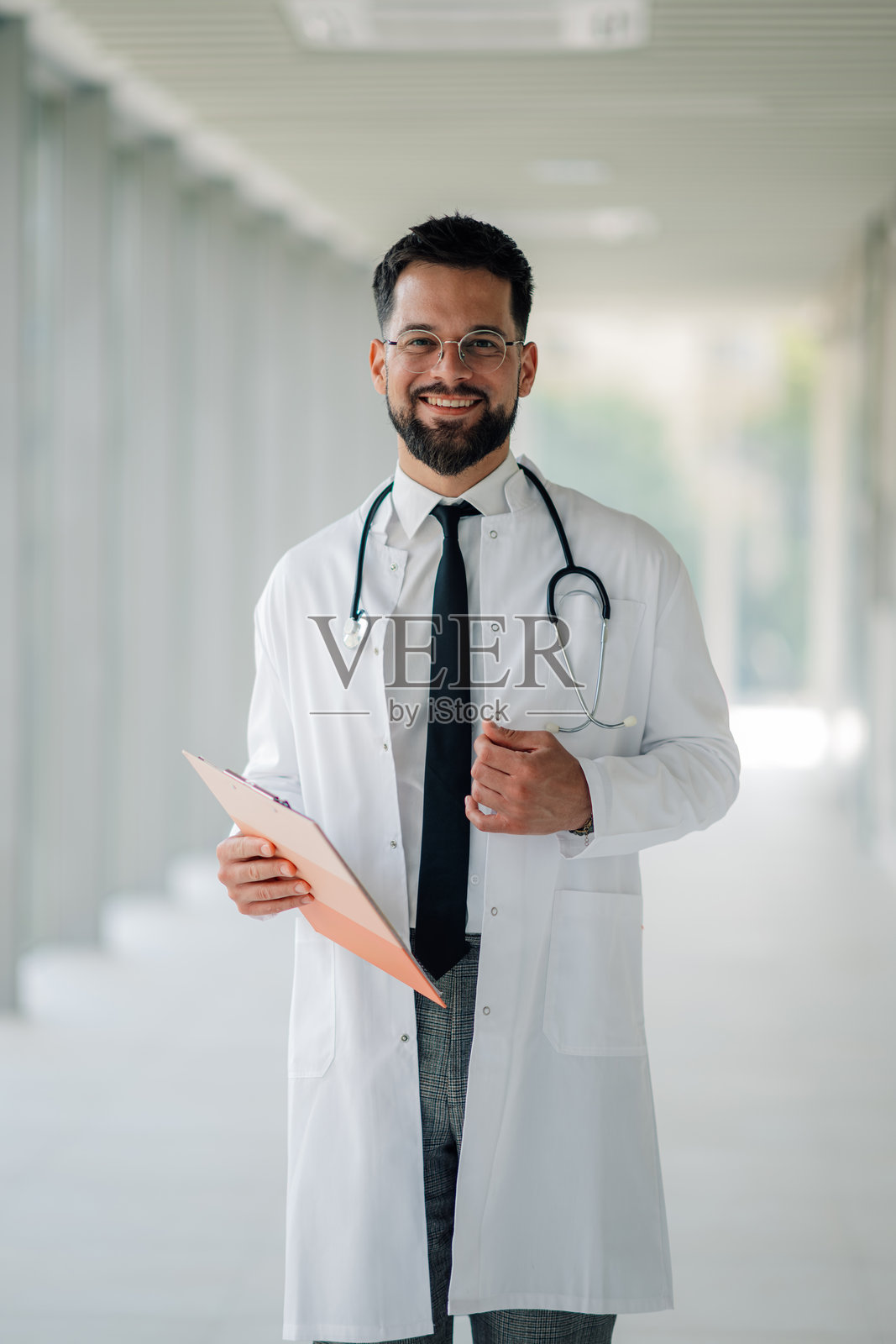 微笑的医生在医院走廊中手持病人病历的肖像照片摄影图片