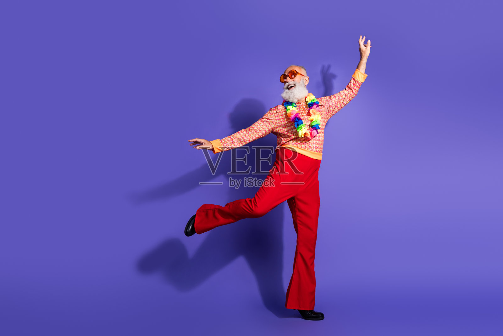 充满魅力的老年男子穿着复古风格的迪斯科服装，在紫色的摄影棚背景下充满活力地跳舞照片摄影图片
