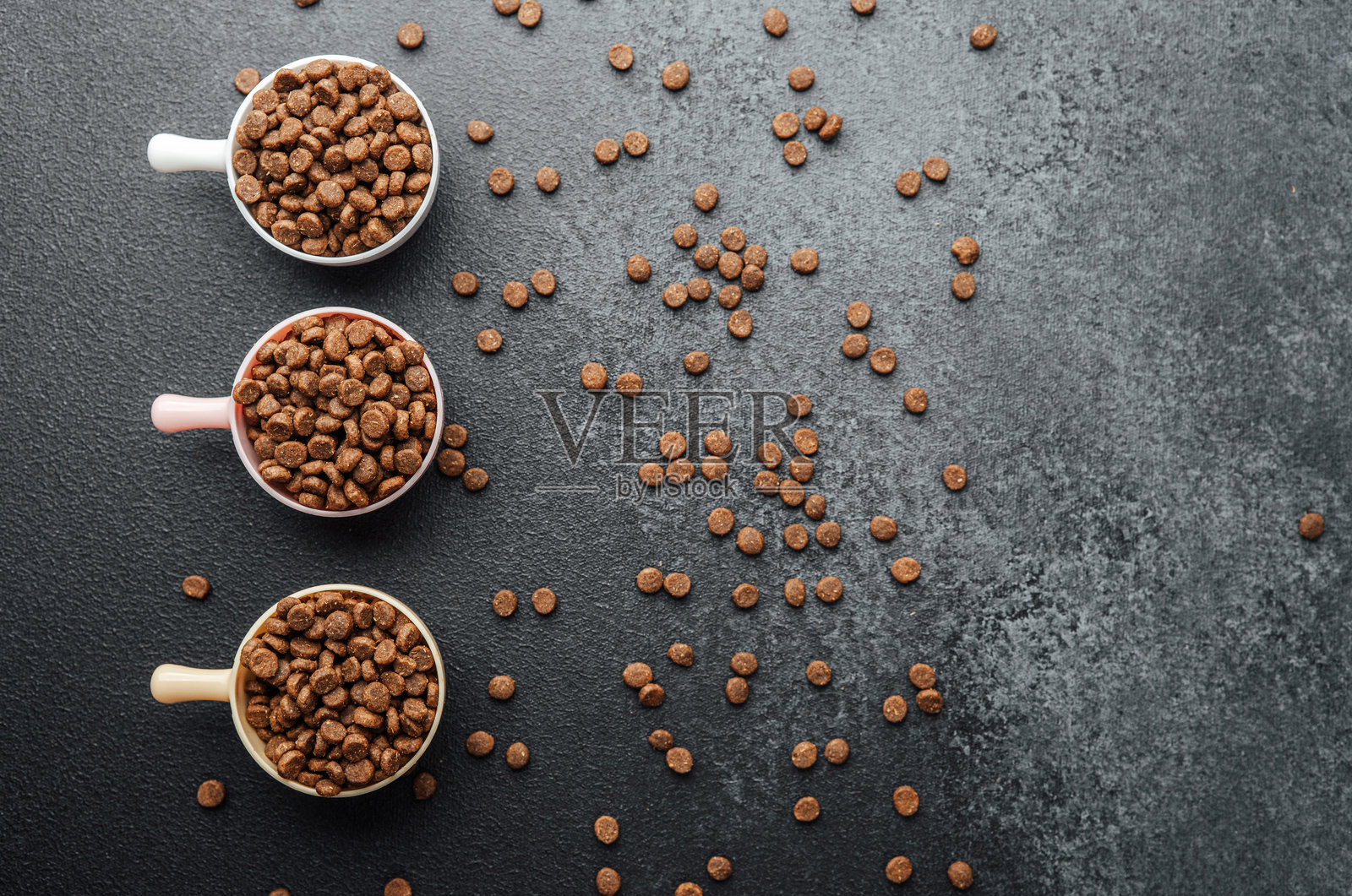 三碗干狗粮放在黑色纹理背景上，周围散落着狗粮颗粒照片摄影图片