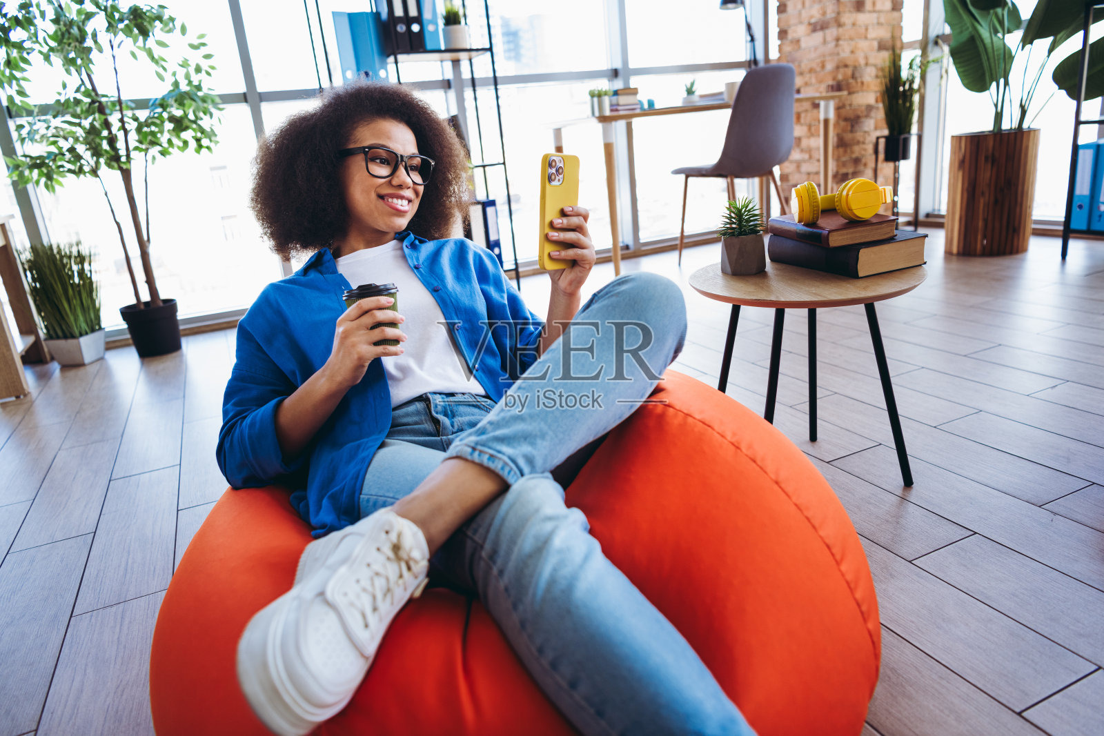 年轻职业女性在现代办公室环境中放松，手持智能手机。照片摄影图片