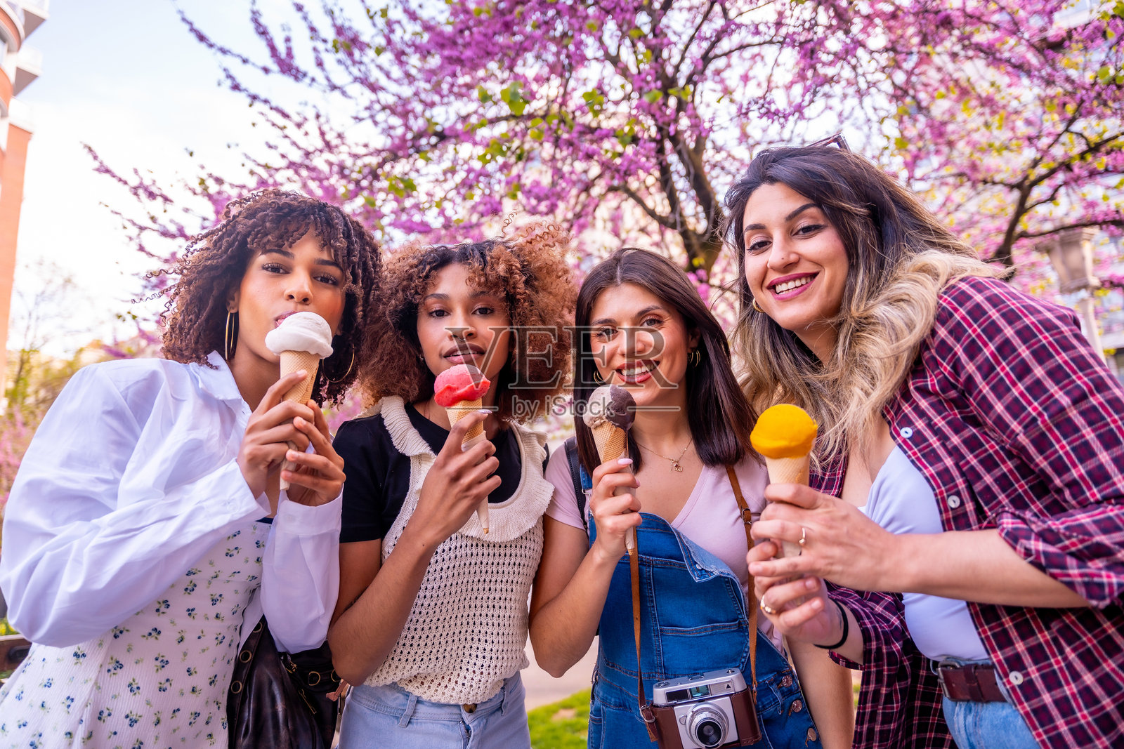 四位年轻女性在盛开的树下吃冰淇淋蛋筒照片摄影图片
