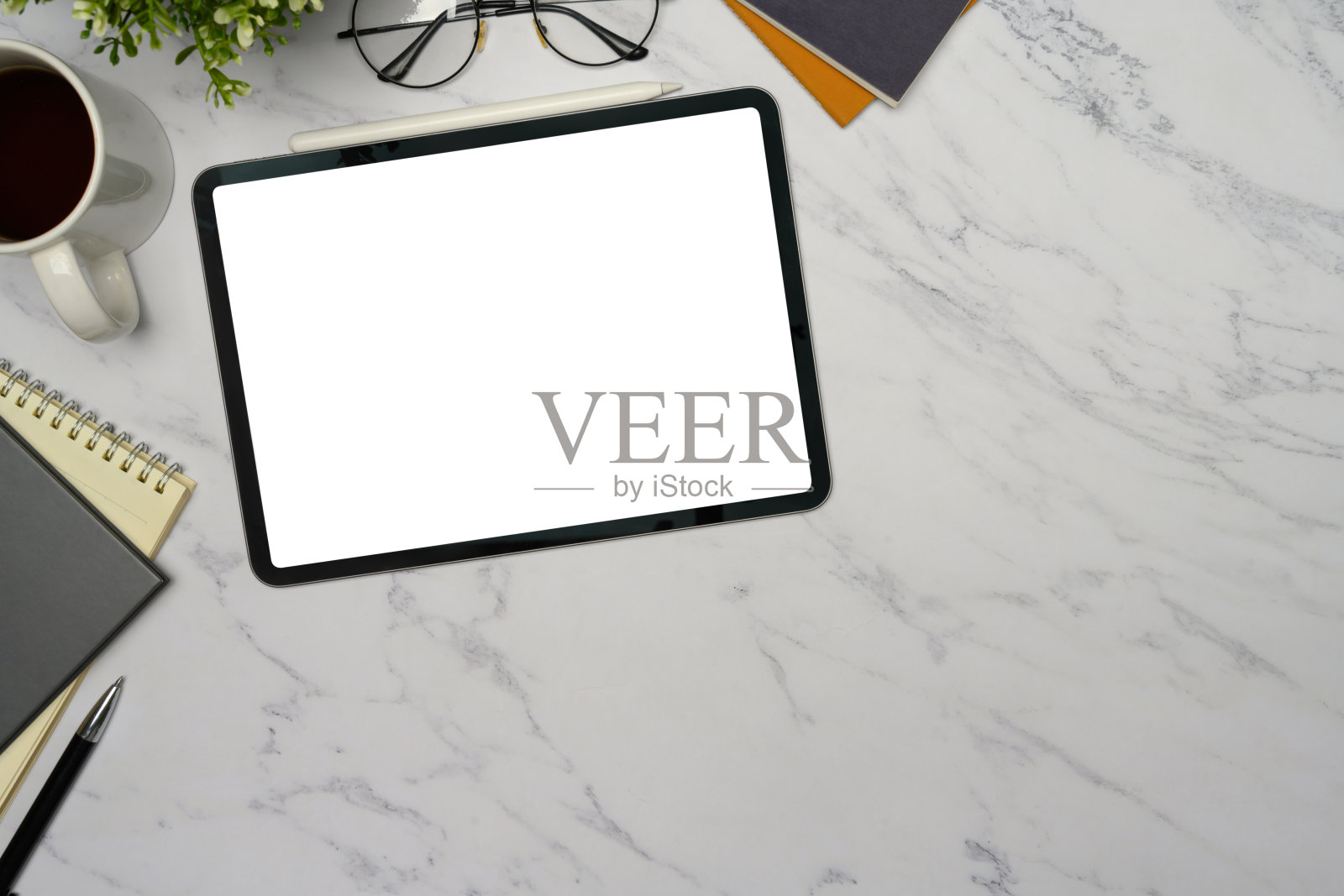 大理石桌面上的数字平板，白色屏幕空白，周围有咖啡、眼镜和笔记本。照片摄影图片