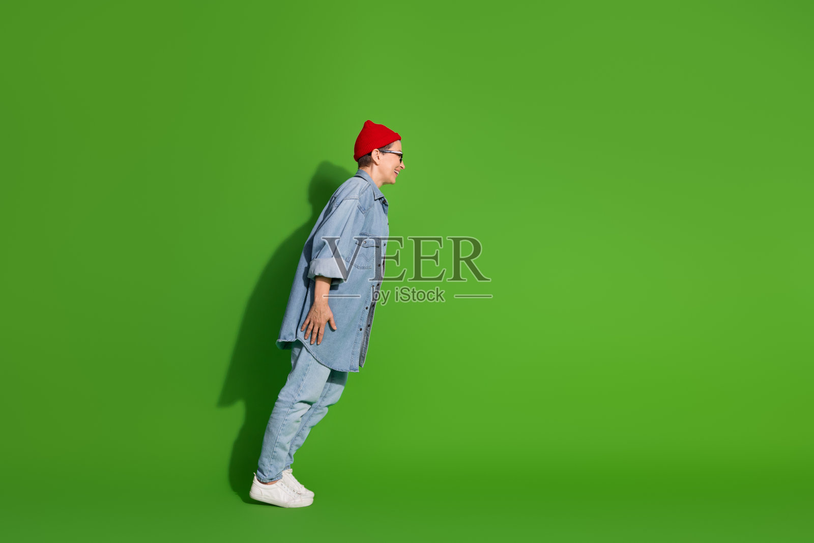 时尚的成熟的女性穿着牛仔服，俏皮地向前倾靠在生机勃勃的绿色背景上照片摄影图片