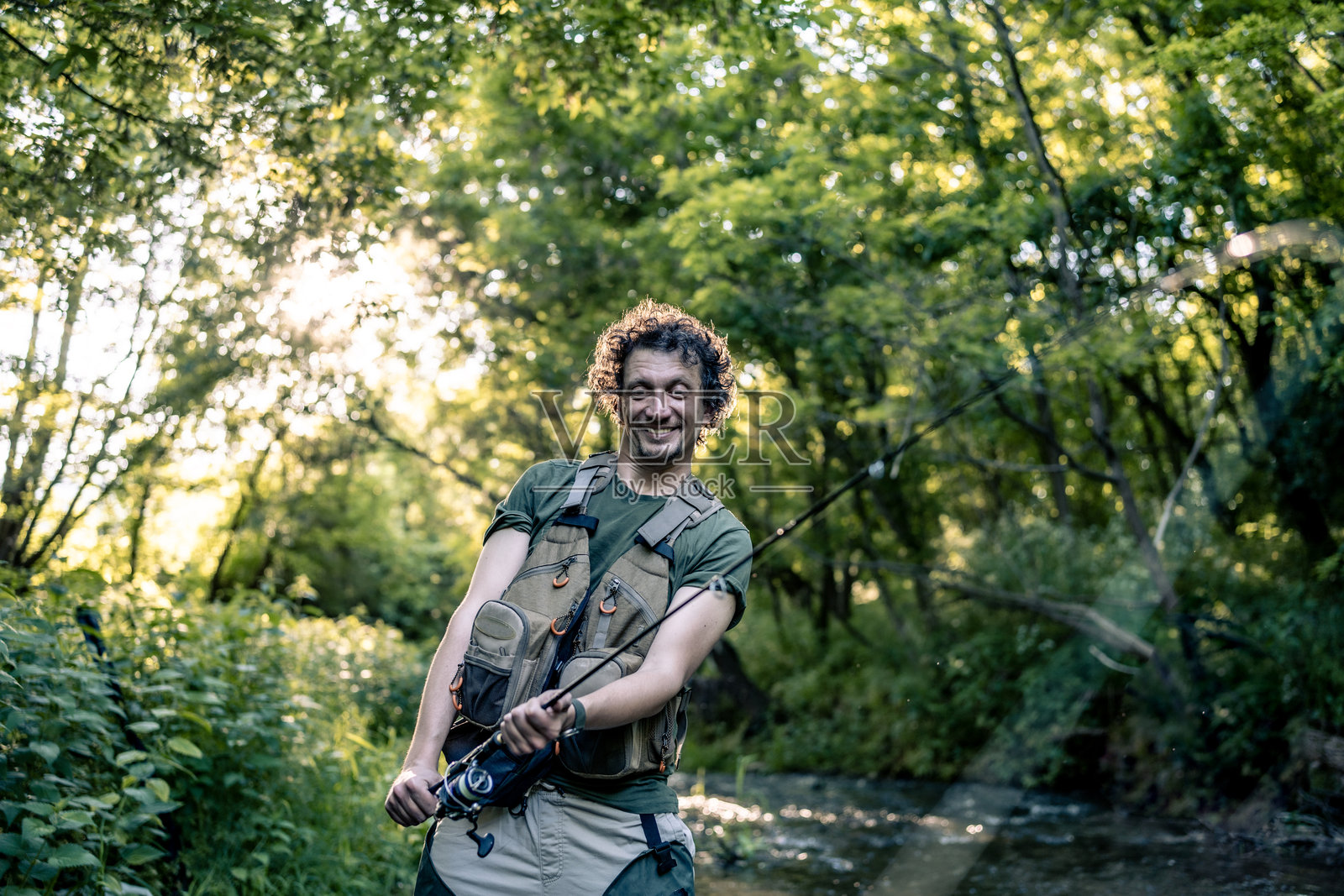 男子在阳光明媚的日子里享受在森林溪流附近的休闲钓鱼照片摄影图片