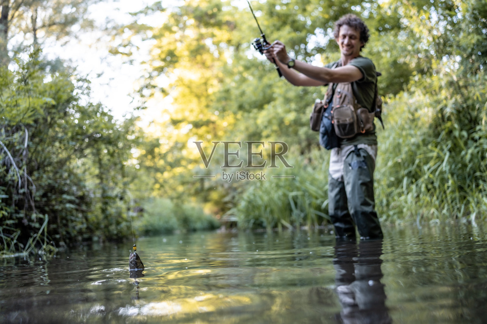 阳光明媚的日子里，男人在宁静的河流环境中钓鱼照片摄影图片