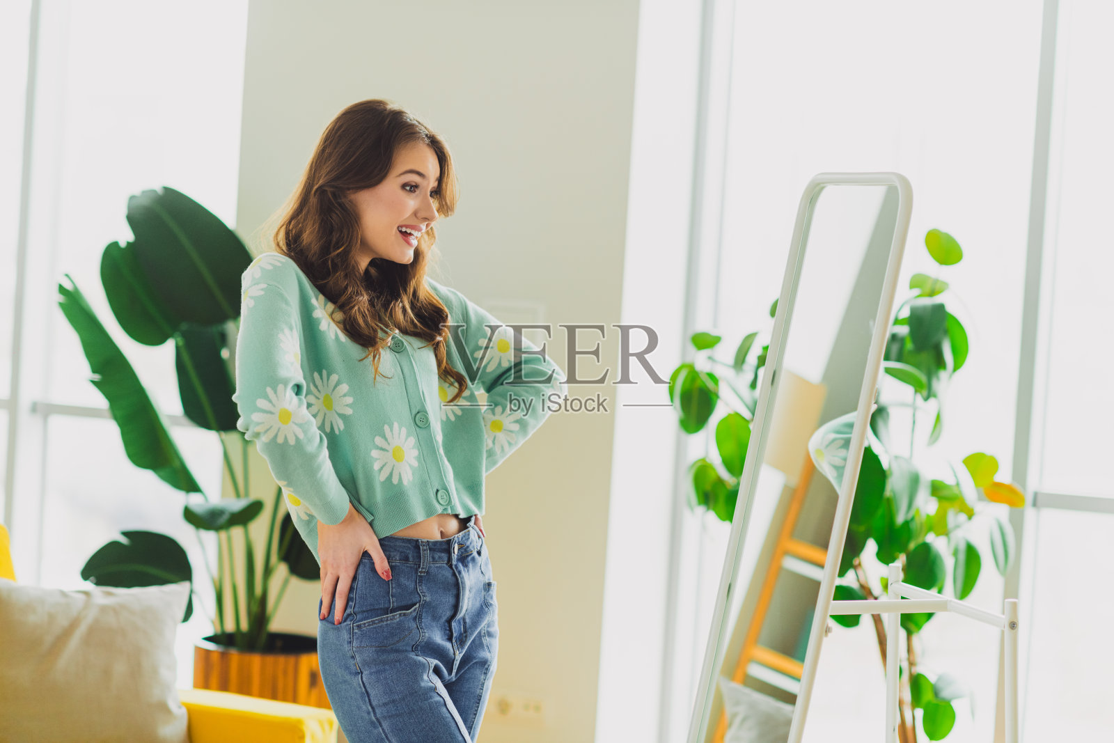 一位深色头发的女性在现代装饰的舒适客厅中欣赏自己的倒影，穿着一件愉快的绿色开衫。照片摄影图片