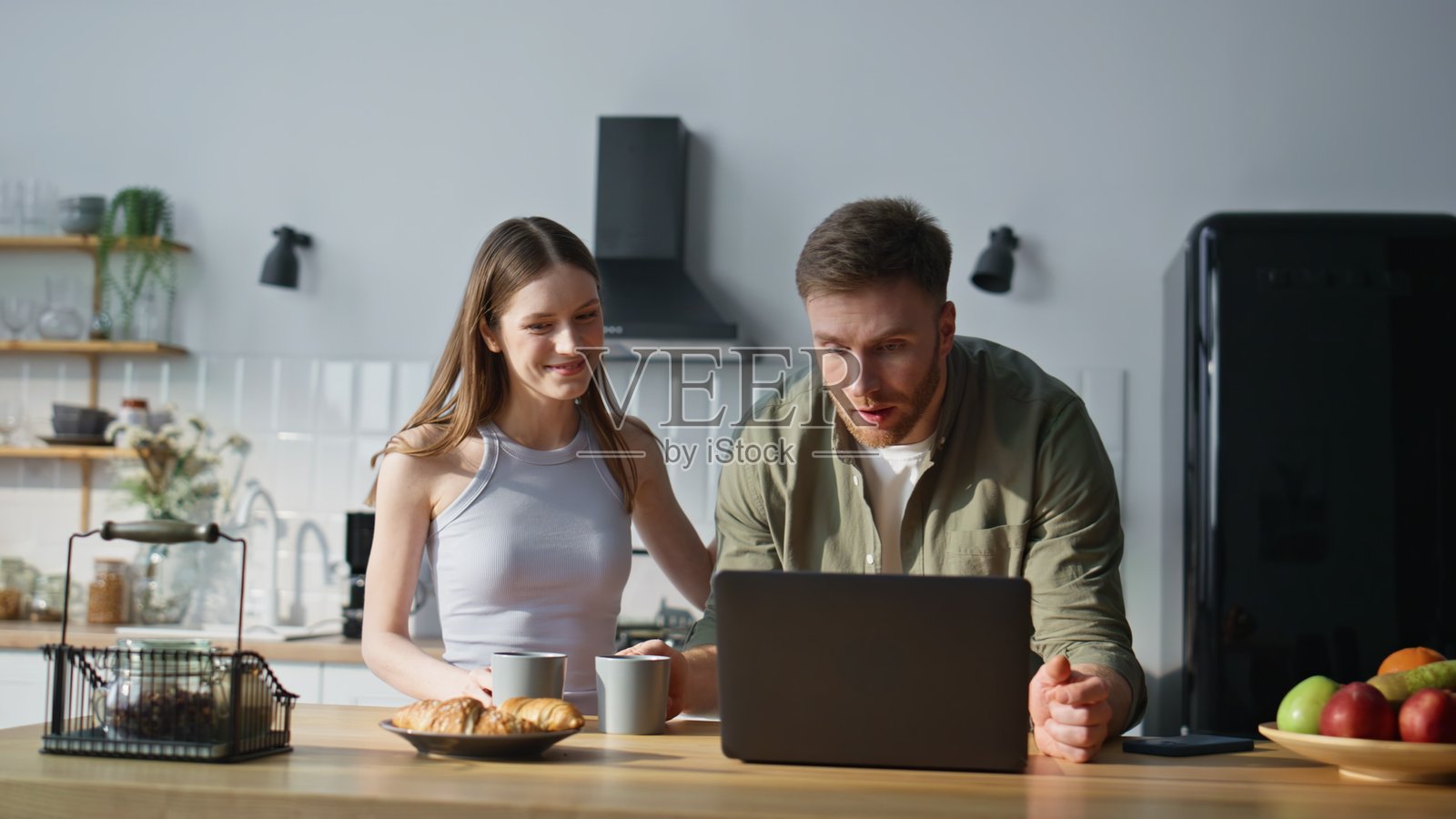 丈夫在家厨房亲吻告别妻子，妻子手里拿着咖啡杯，微笑着。照片摄影图片