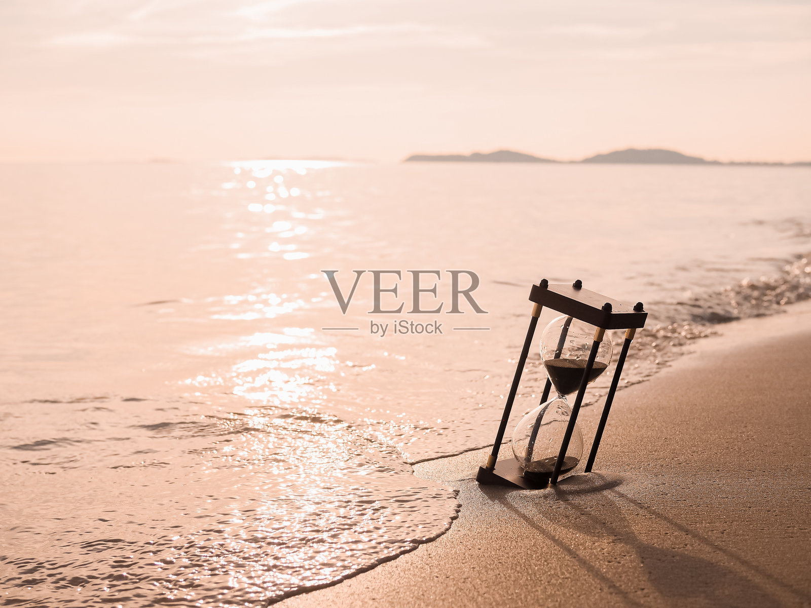 沙滩上的沙漏在日落时分。关于夏季、旅行、假期和放松的倒计时概念。照片摄影图片