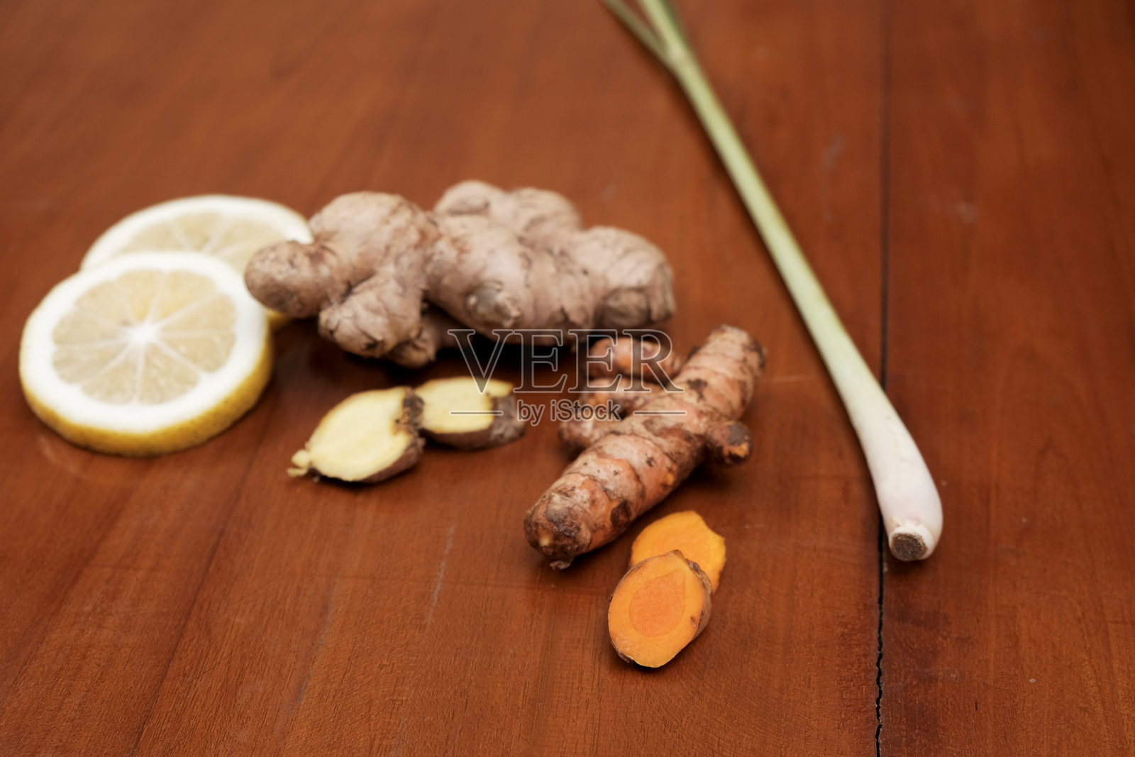 木桌上放着姜黄、生姜、切片柠檬和香茅，用于制作草药饮品。照片摄影图片