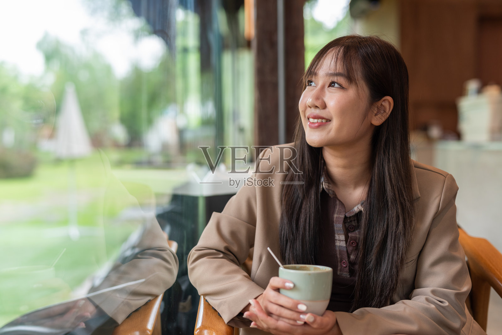 女人在咖啡馆喝咖啡，透过窗户看外面。照片摄影图片