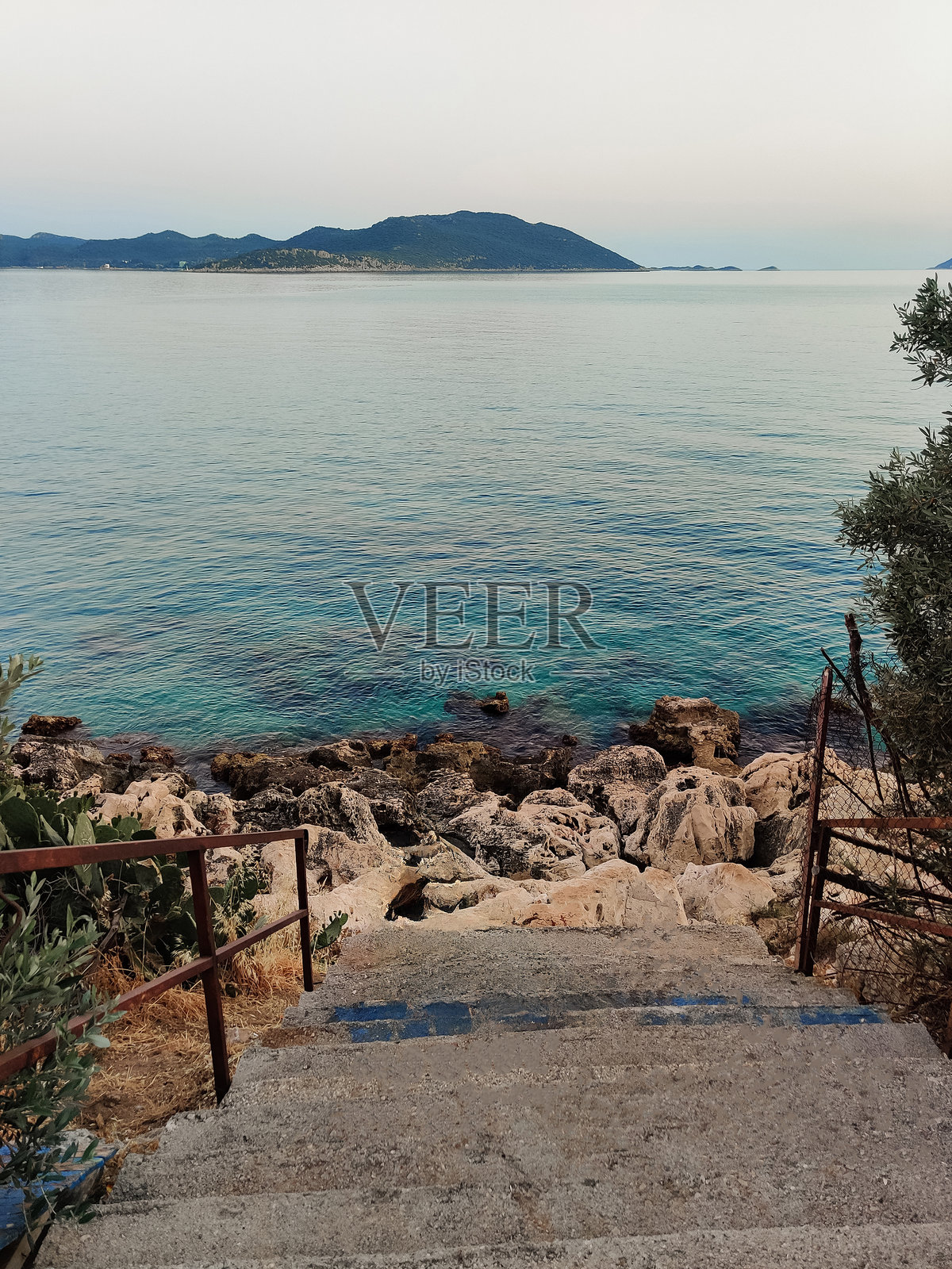 一个美丽的女孩坐在楼梯上，望着大海。照片摄影图片