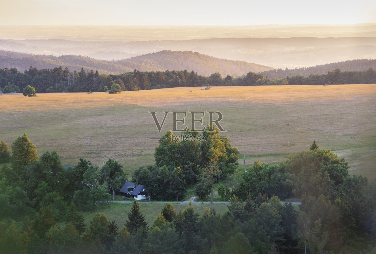 典型的波兰乡村老小屋，四周环绕着美丽的绿树，落叶树和针叶树。风景被山丘环绕（苏台德山，下西里西亚省，波兰）。日落的色彩。照片摄影图片