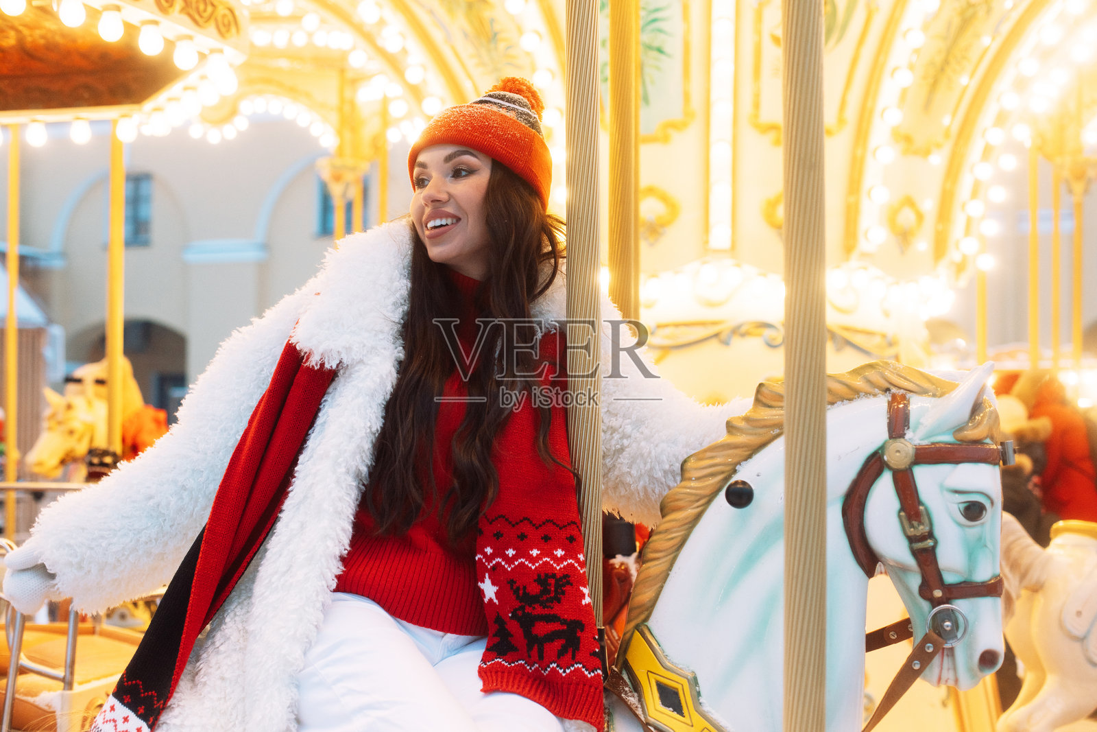 美丽的棕发女性在旋转木马上。模特骑在马背上，在冬季假期中尽情玩乐。照片摄影图片