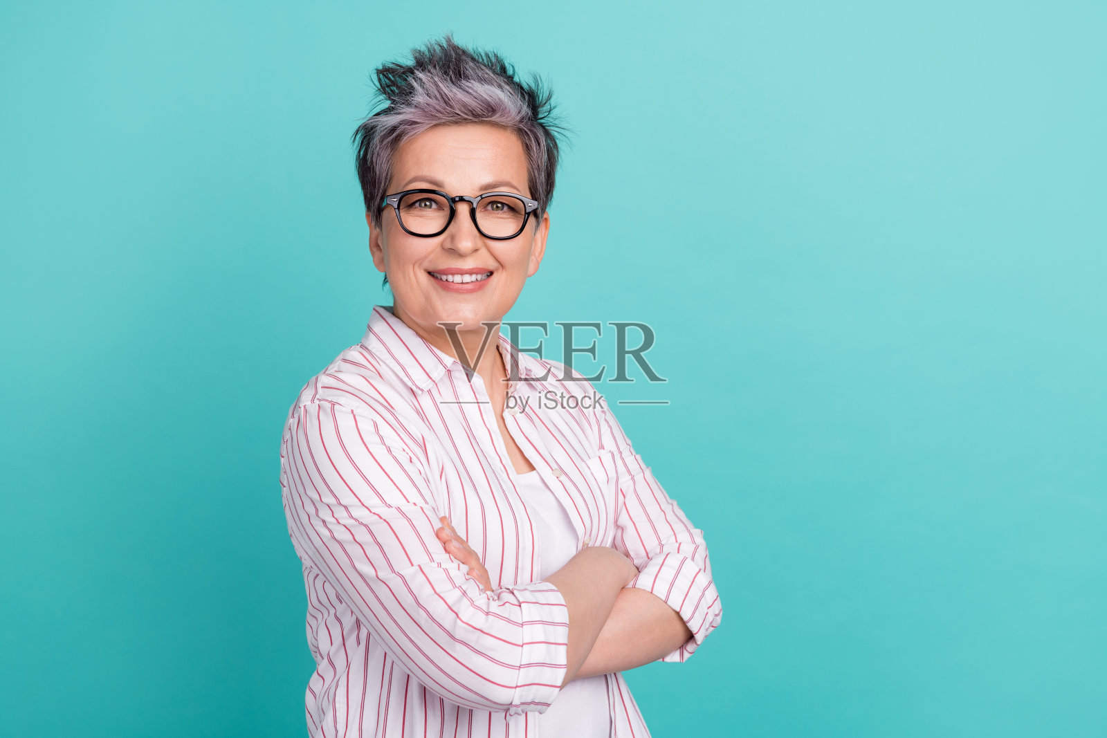 迷人的年长女商人站在空旷的地方，双臂交叉，背景为青色。照片摄影图片