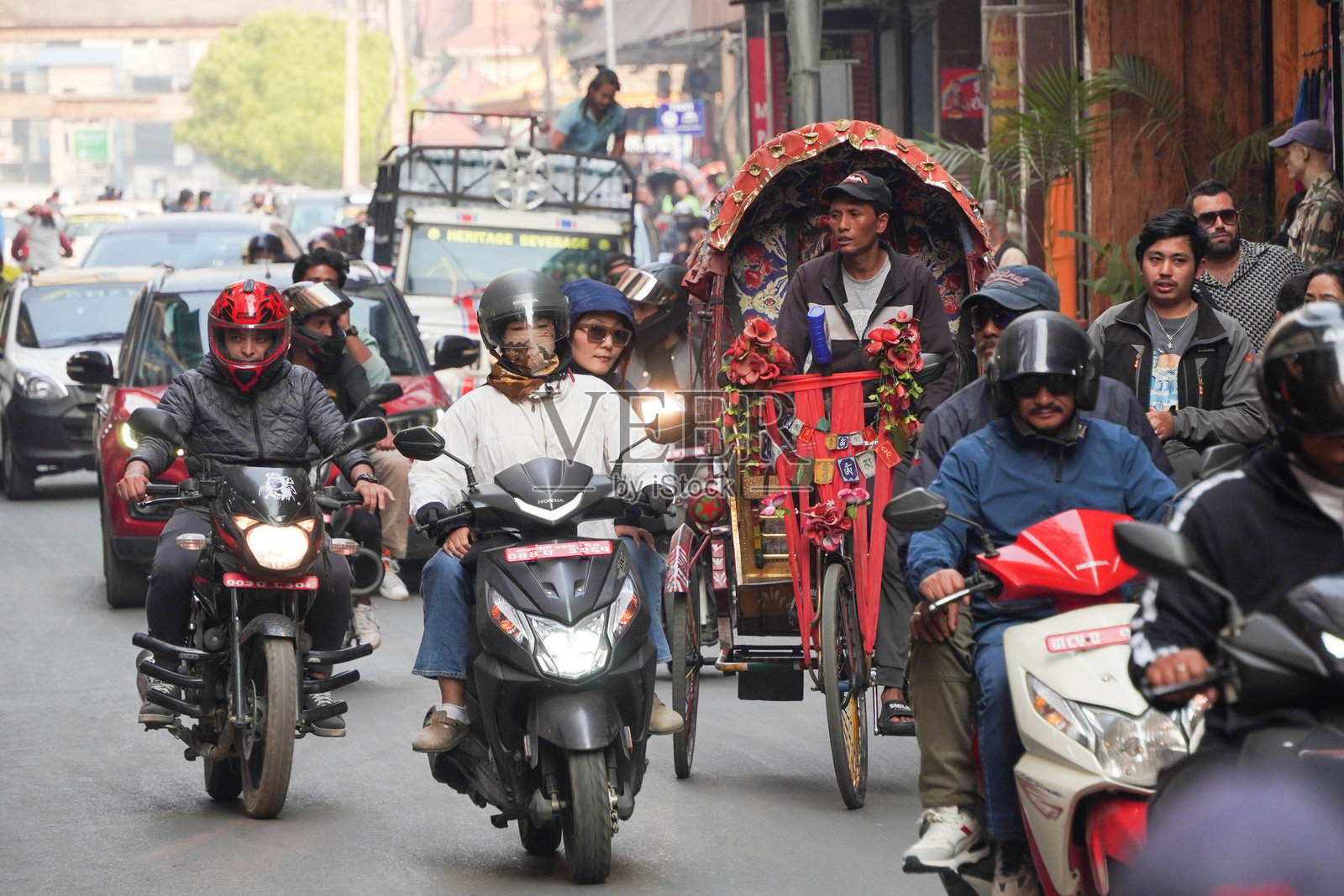 加德满都街头的尼泊尔传统人力车在繁忙的交通中穿行，周围是密集人口区的多层建筑。照片摄影图片