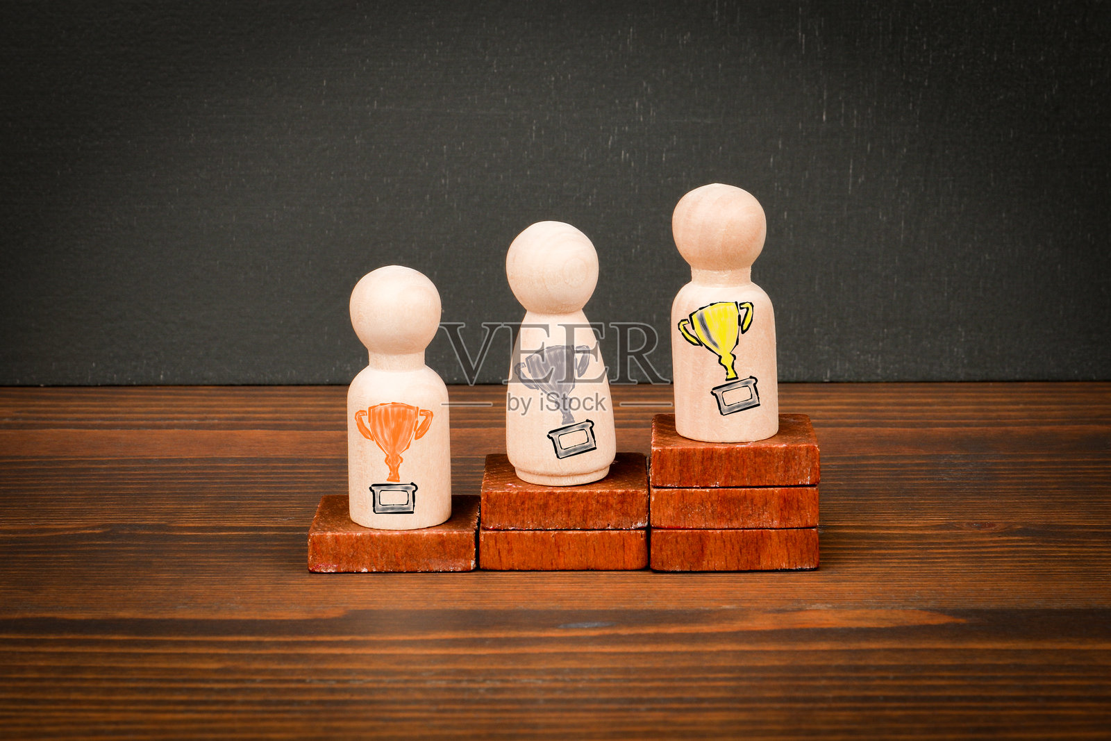 木制人物在讲台上代表第一、第二和第三名，旁边有奖杯符号照片摄影图片