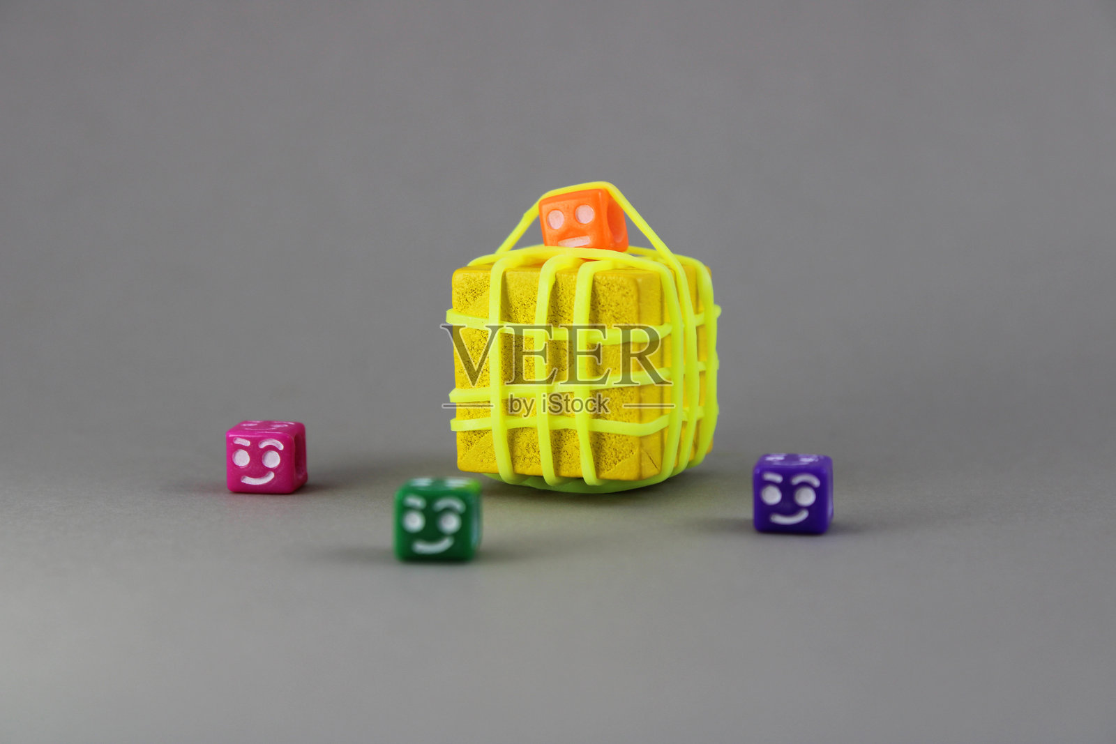 一个带有悲伤面孔的立方体被橡皮筋困住，周围是其他自由的带有快乐面孔的立方体。照片摄影图片