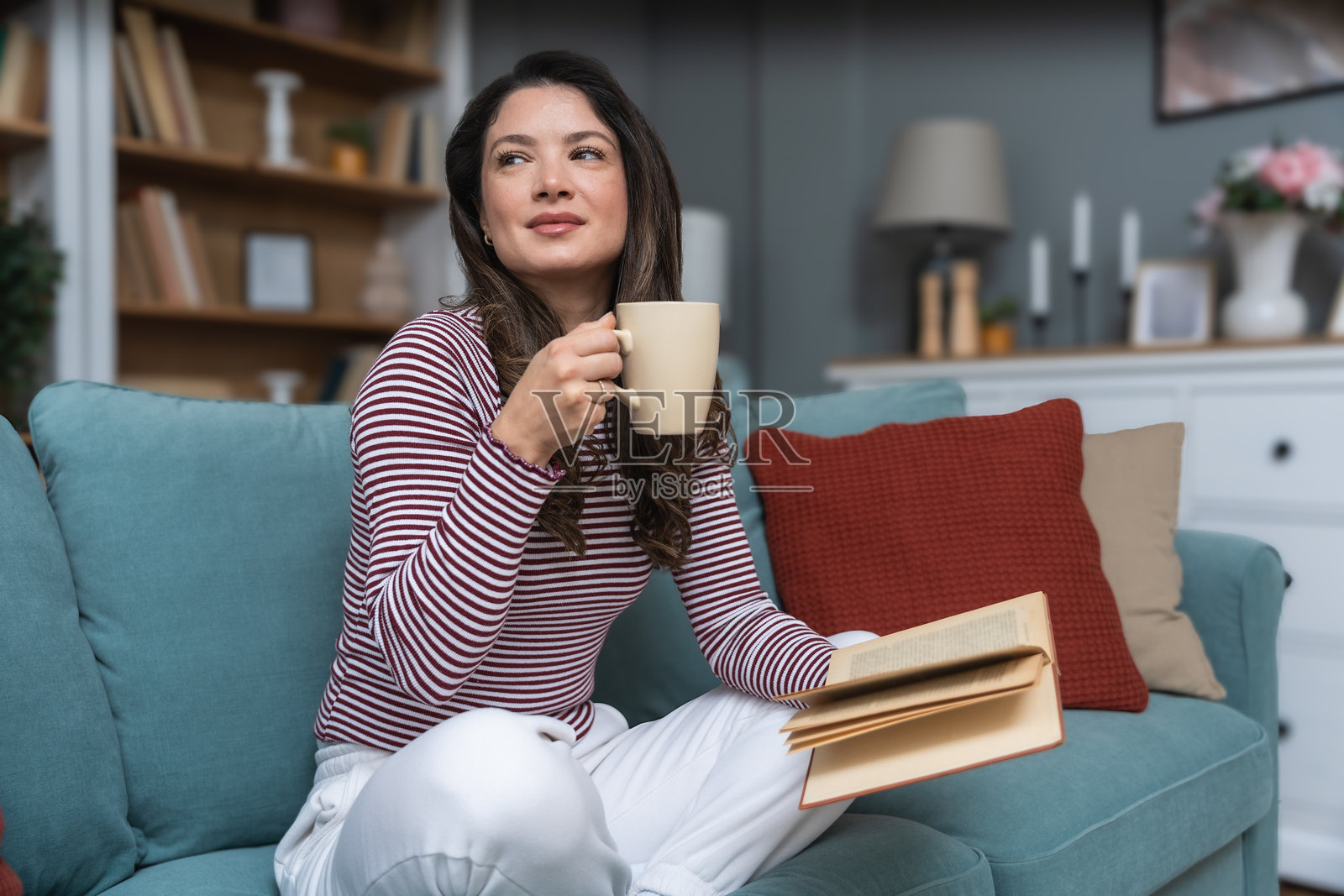 生活平衡、自尊心、心理健康和独立性。一位年轻女性坐在她的小现代家中，喝着咖啡，阅读一本书。她保持心理稳定，并不断自我教育。照片摄影图片