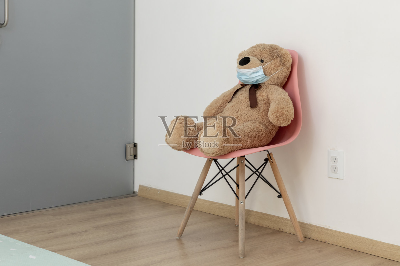 戴着防护口罩的泰迪熊坐在医生办公室的椅子上照片摄影图片