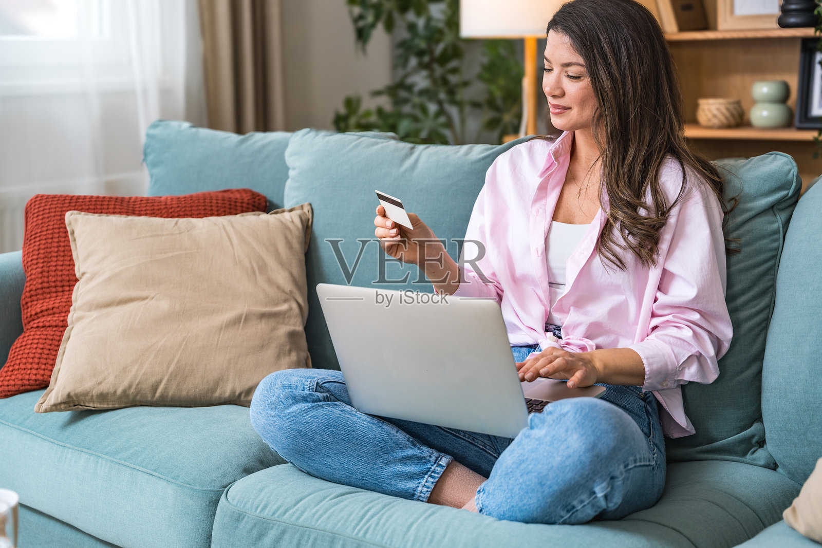 消费主义与购物成瘾。年轻女性坐在家中的沙发上，使用信用卡在线购买不需要的物品。沉迷于购物，超支消费。心理上的依赖。照片摄影图片
