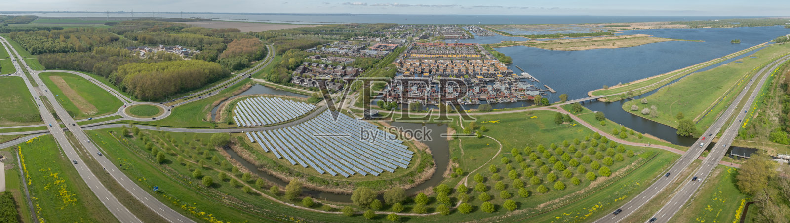 荷兰阿尔梅勒附近现代住宅区和环路旁的绿色景观中，呈岛屿形状的太阳能发电厂全景，展示了有交通的道路。照片摄影图片