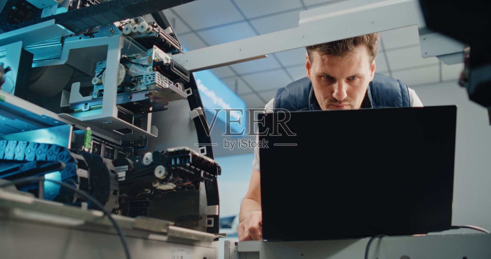 穿着制服的男性技术人员正在使用笔记本电脑设置和维护自动取款机照片摄影图片