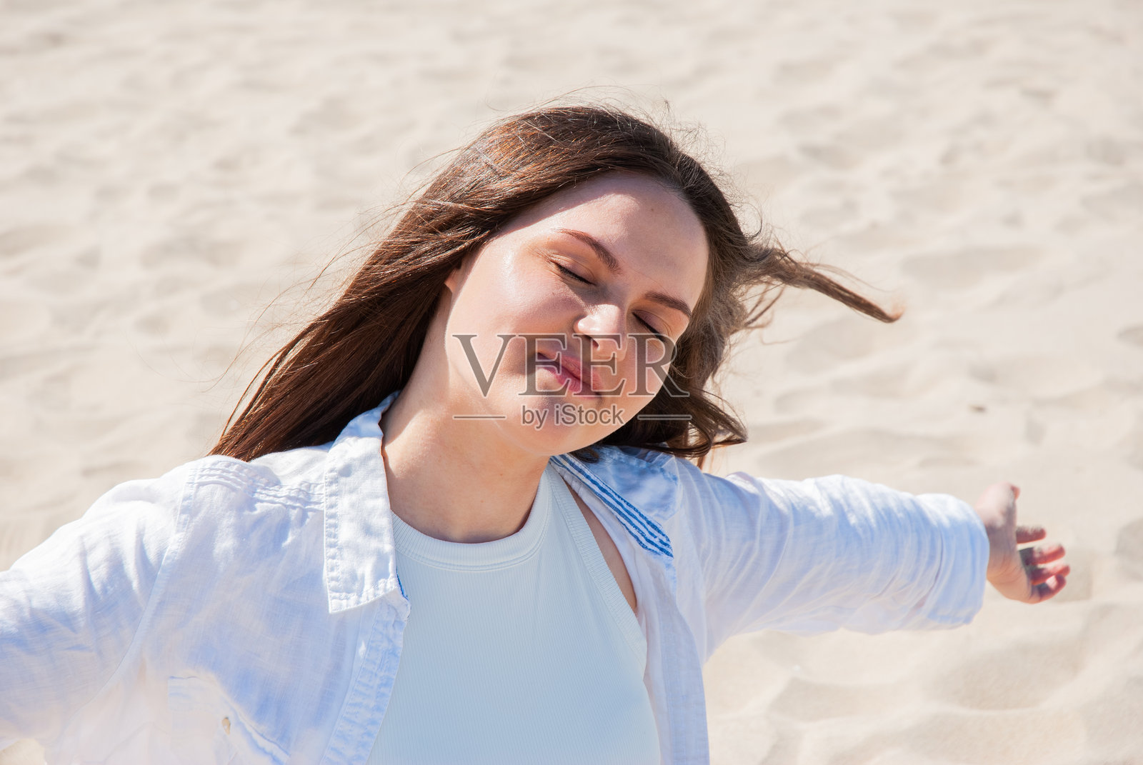 年轻的白人女性在沙滩上享受阳光，双臂张开，闭着眼睛，尽情拥抱放松与自由。数字游牧生活方式。远程工作。照片摄影图片