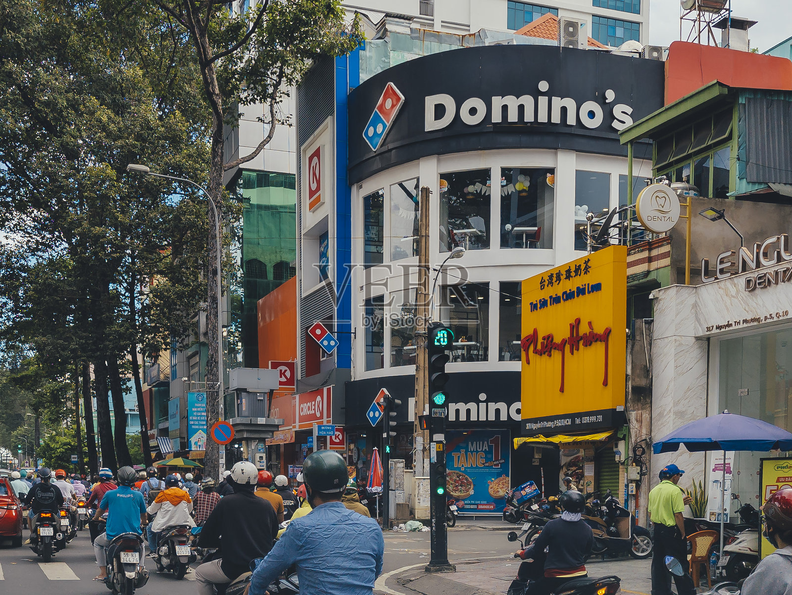 城市街景，电动车和行人在中午交通繁忙的阮志芳街上，视野中有Circle K和Domino's Pizza。照片摄影图片