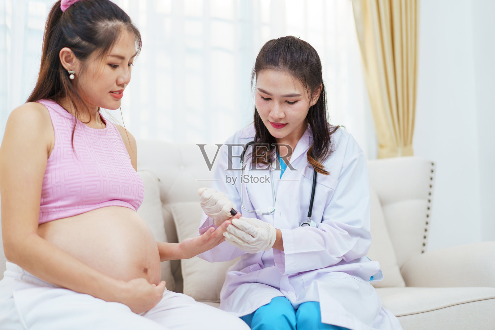 亚洲孕妇在产前检查中与医生使用血糖仪进行血糖测试。照片摄影图片