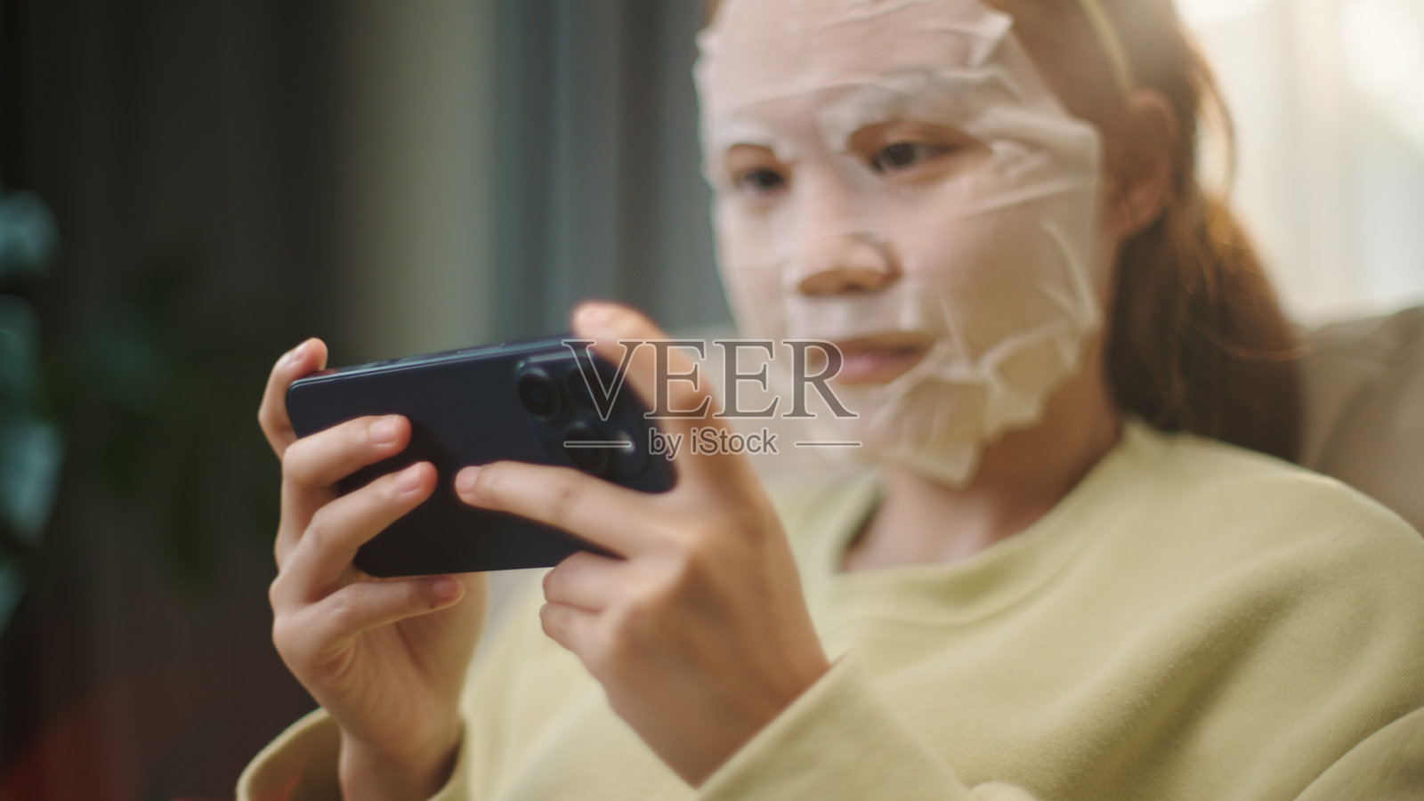 戴着面膜的青少年在玩智能手机游戏。照片摄影图片