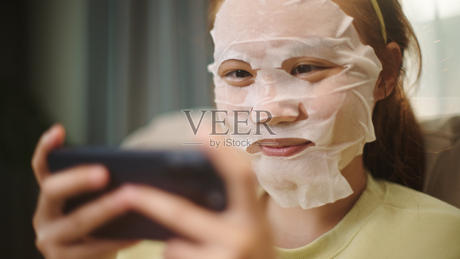 戴着面膜的青少年在玩智能手机游戏。照片摄影图片