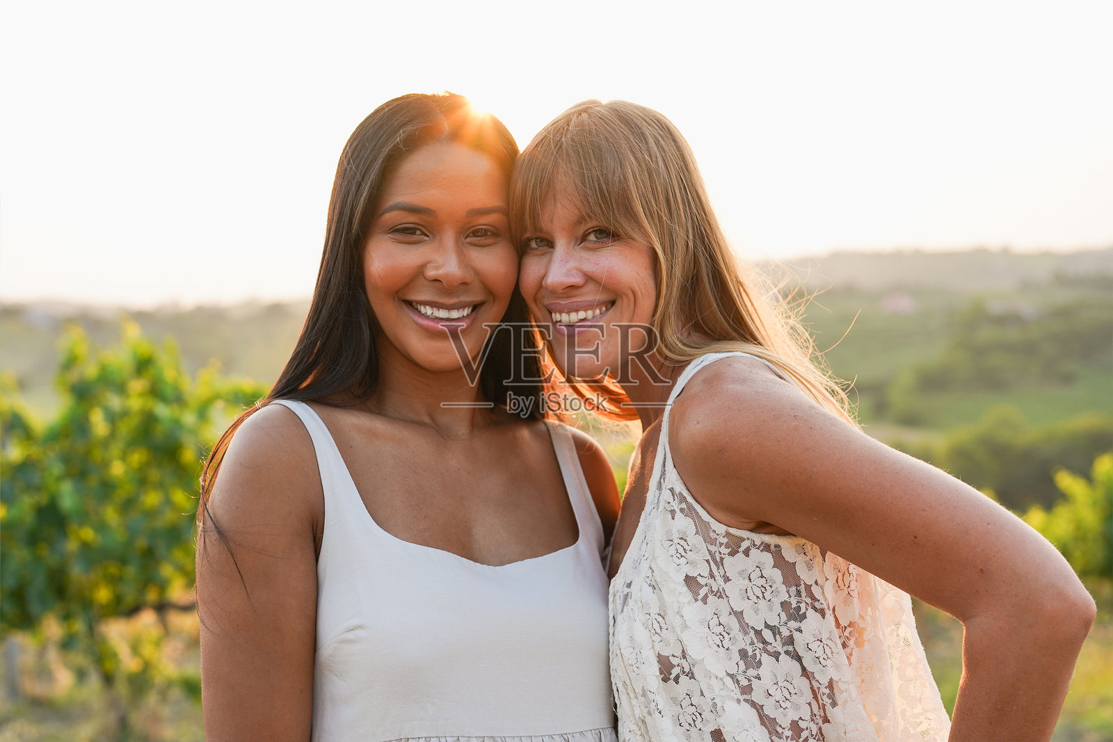 快乐的年轻多种族女性在夏季的葡萄园里对着镜头微笑 - 女性友谊与自然的概念照片摄影图片