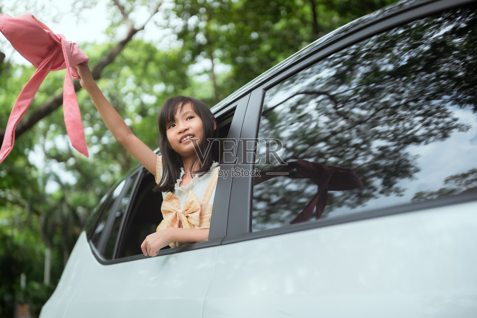 孩子在阳光明媚的日子里，兴奋地把手臂伸出车窗，在绿色公园的环境中享受快乐的旅程。照片摄影图片