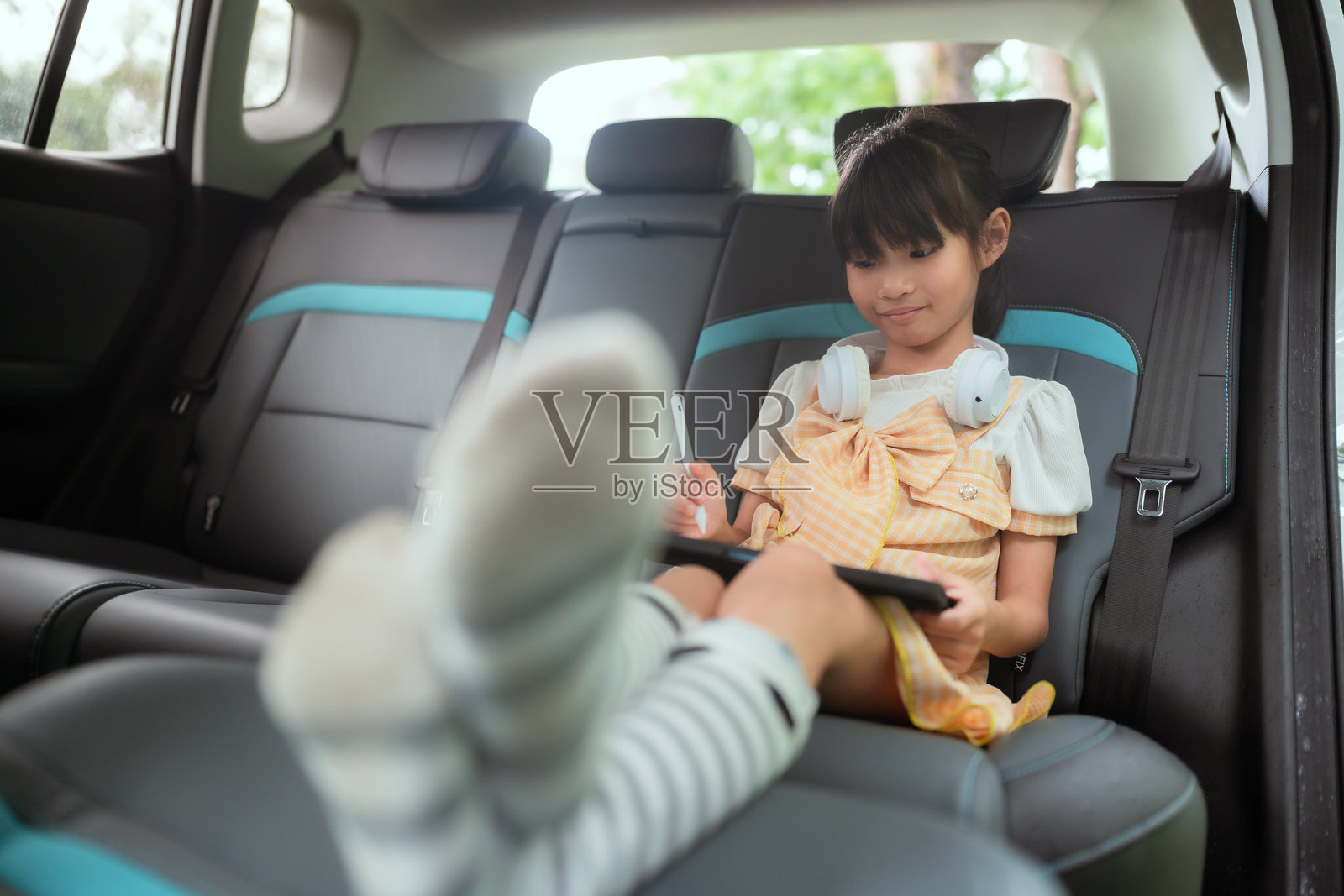小女孩在阳光明媚的下午，放松地坐在车后座上玩平板电脑游戏。照片摄影图片
