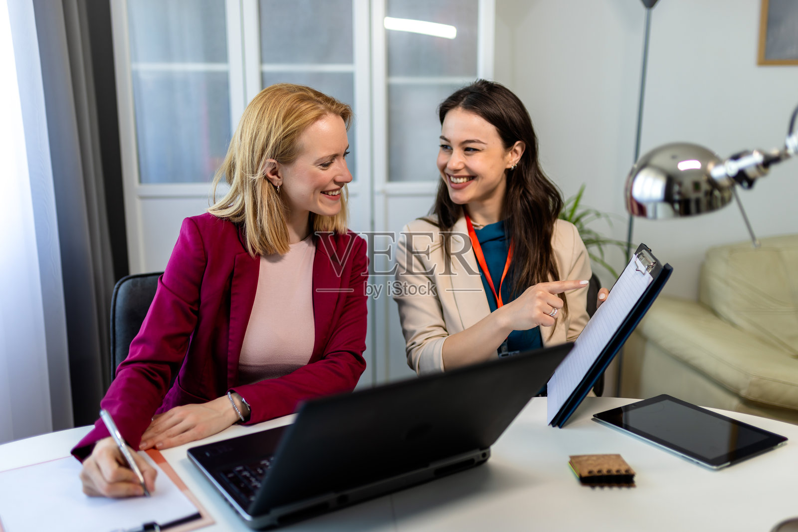 两位年轻女性在家办公时共同使用一台笔记本电脑。照片摄影图片
