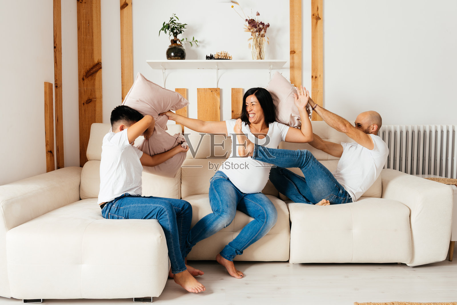 快乐的家庭在家中享受有趣的枕头大战，拥有多元文化背景。照片摄影图片