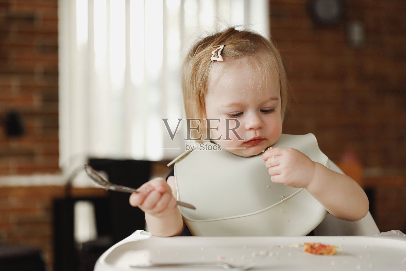 婴儿女孩或幼儿坐在高脚椅上，自己用勺子吃饭。照片摄影图片